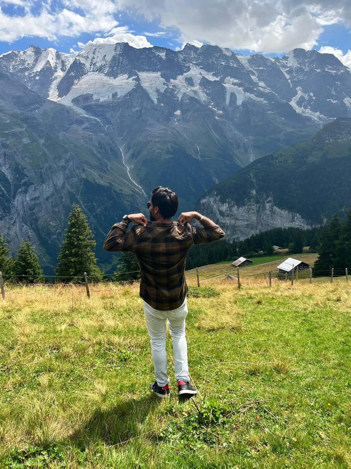 A person standing in a meadow with their back to the camera, looking across to a mountain range.