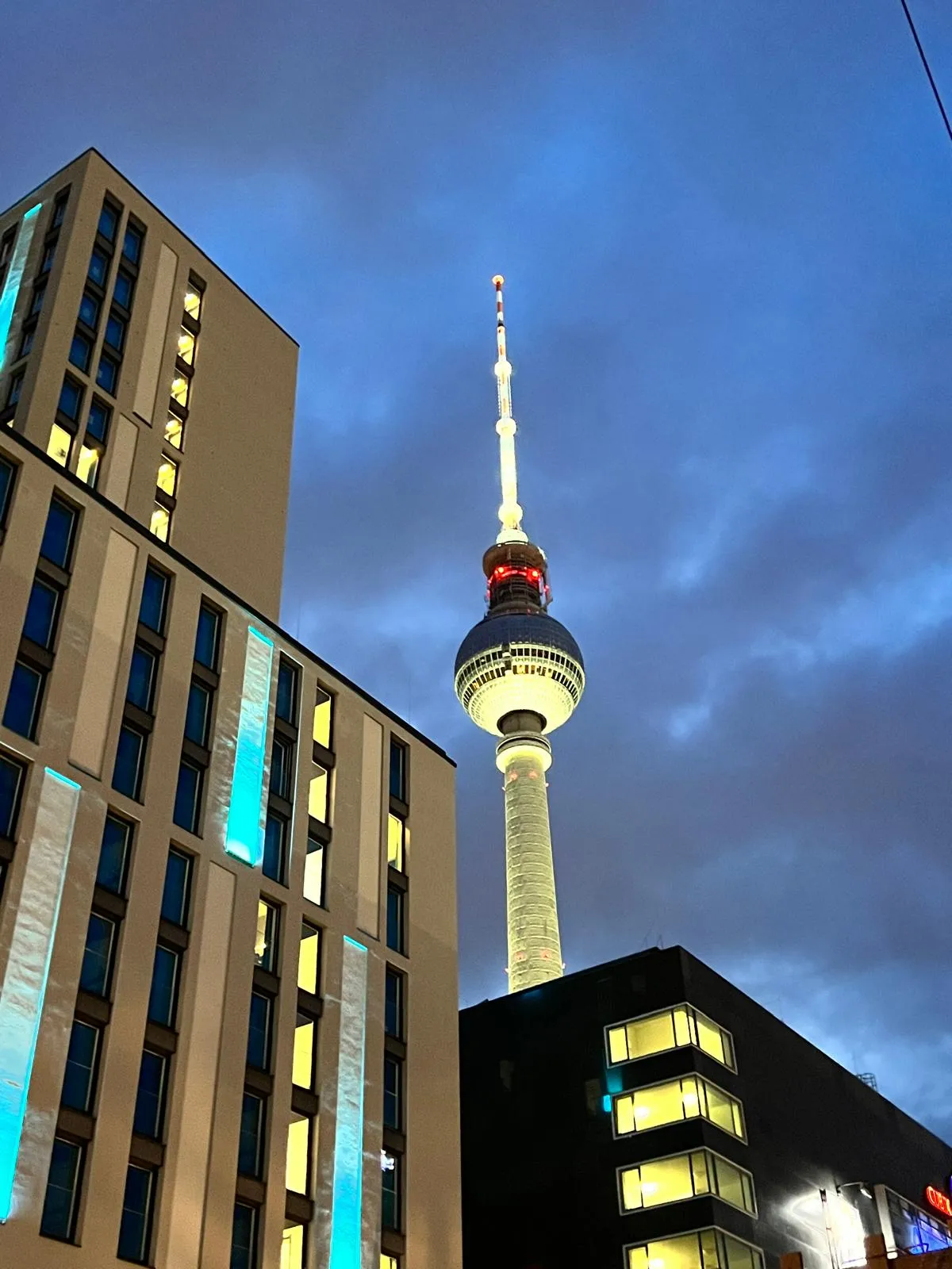 A television tower lit at dusk, seen past the corner of a modern block.