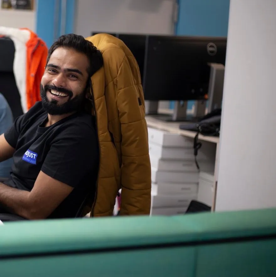 Twinkle Savani laughing in a desk chair, a jacket slung over the back, screens and stacked boxes behind.