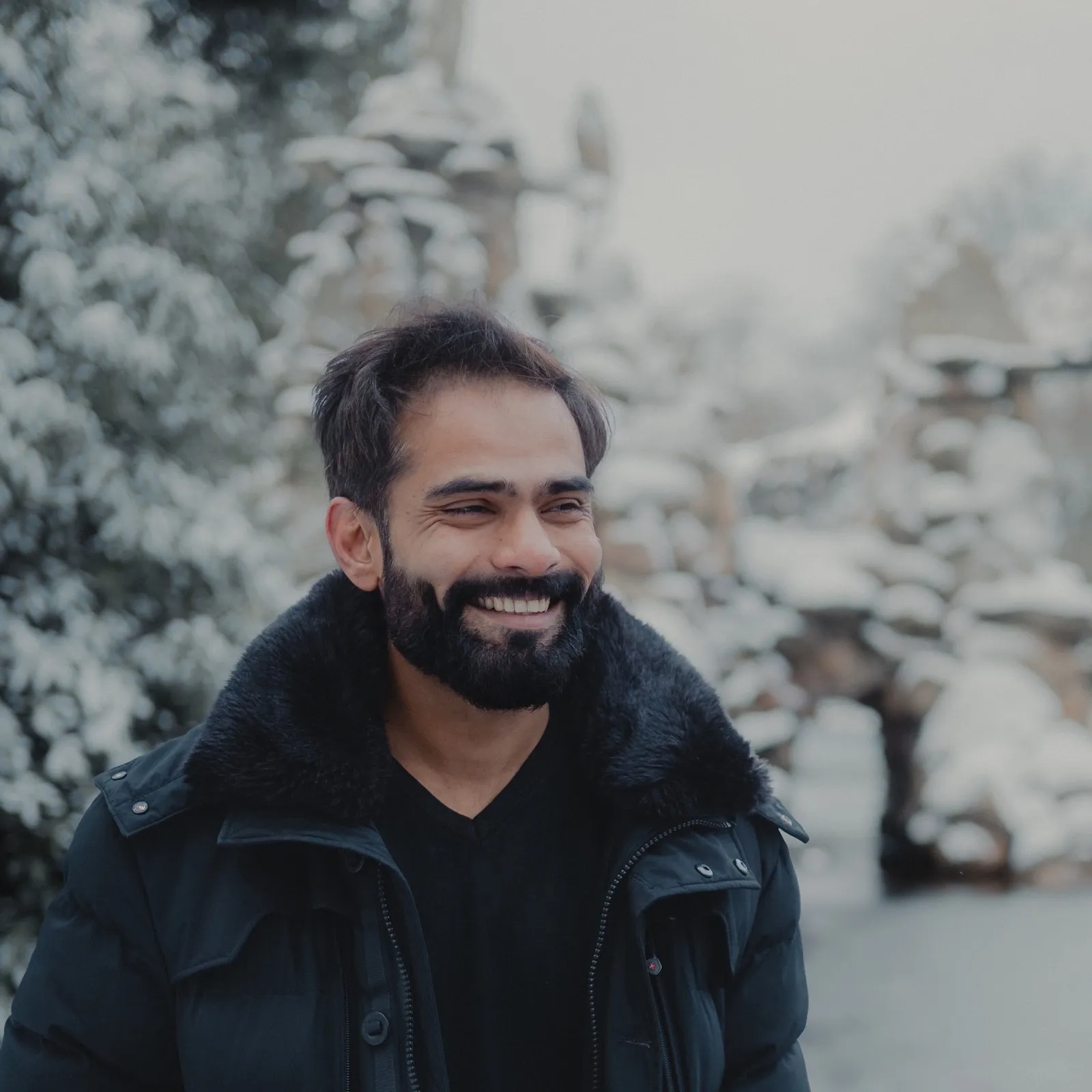 Twinkle Savani laughing and looking away from the camera, on a snow-covered path with a stone arch bridge out of focus behind.